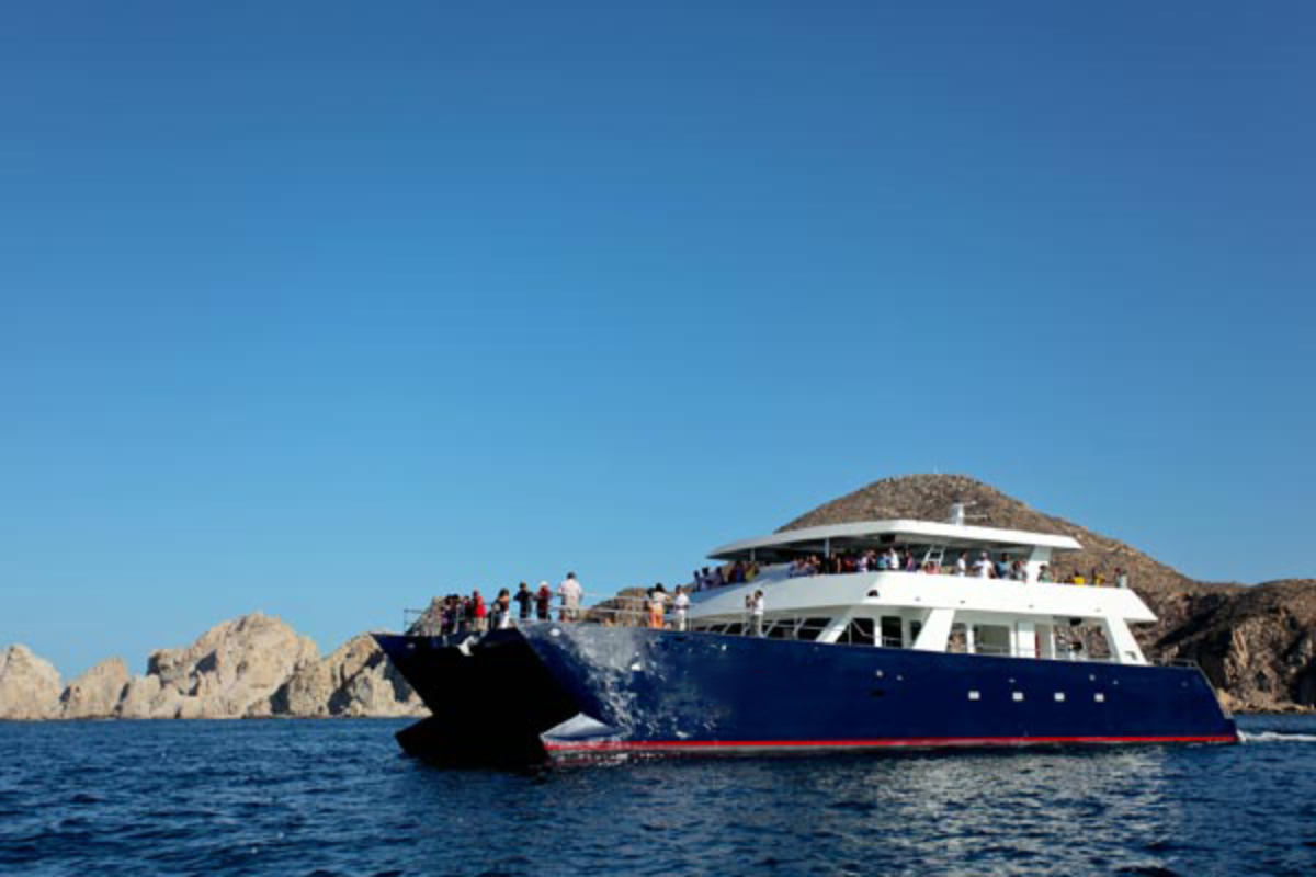 Large blue party catamaran with guests aboard off the Los Cabos coastline
