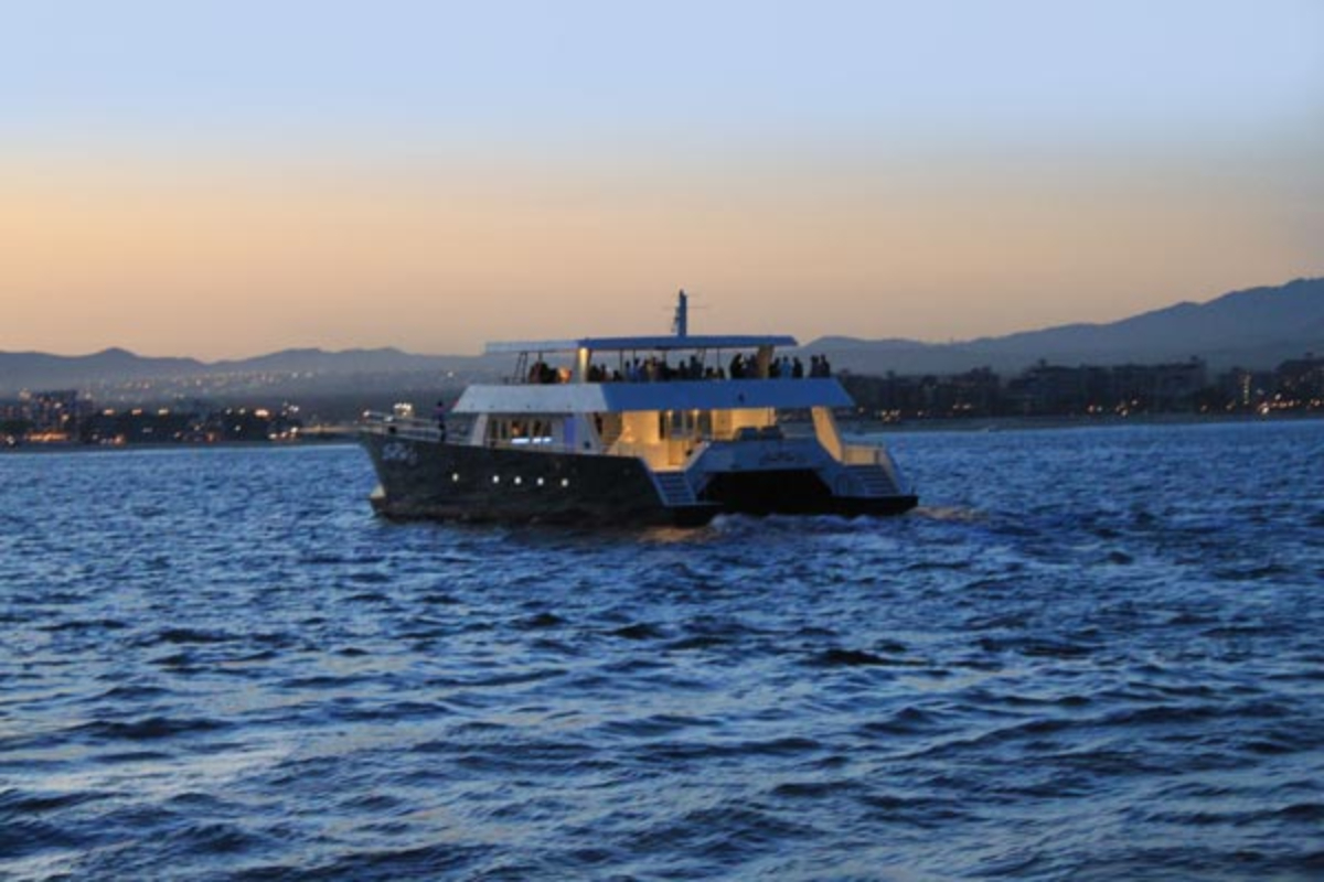 A large event catamaran cruising at dusk with a group on deck