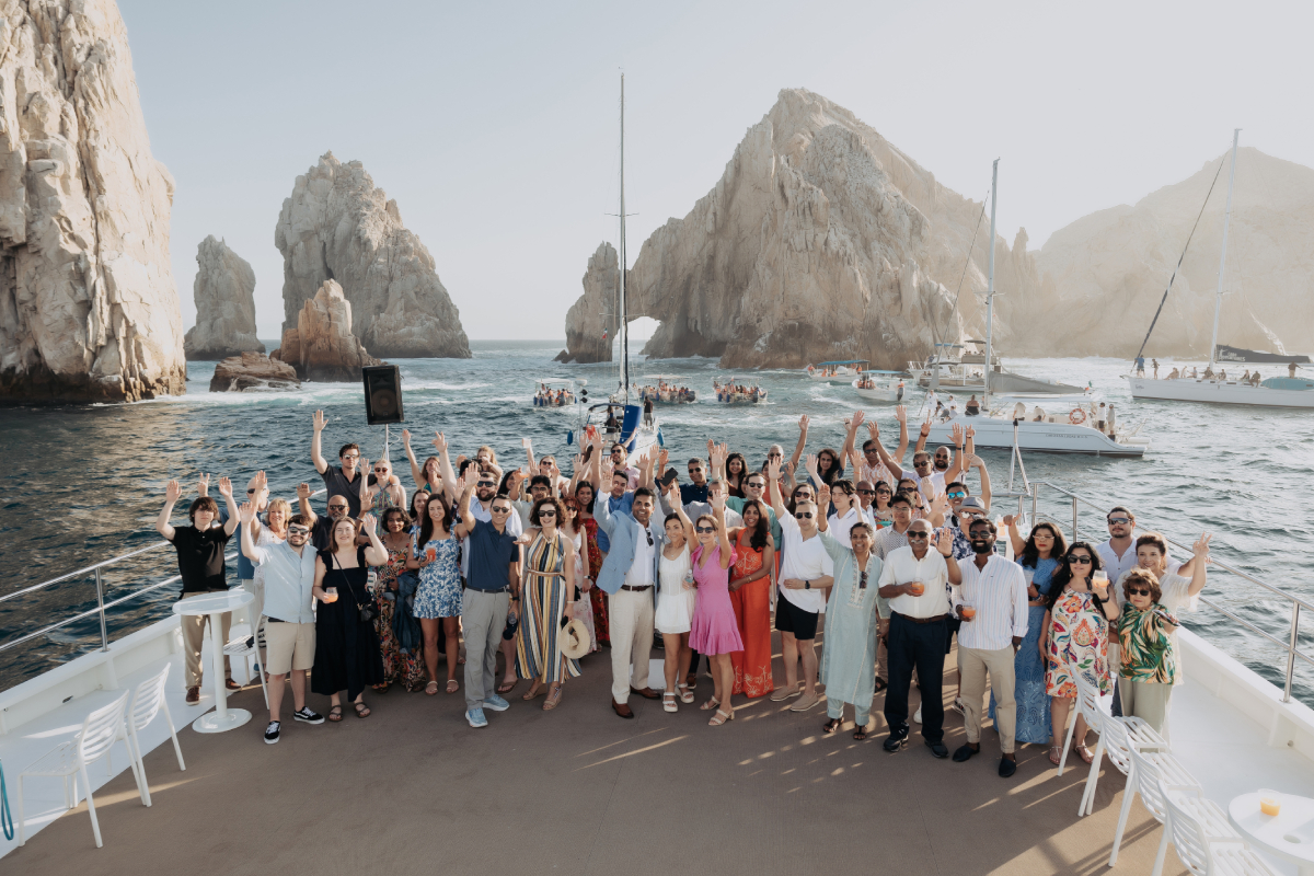 A large celebration group on the deck of a party catamaran near the Arch