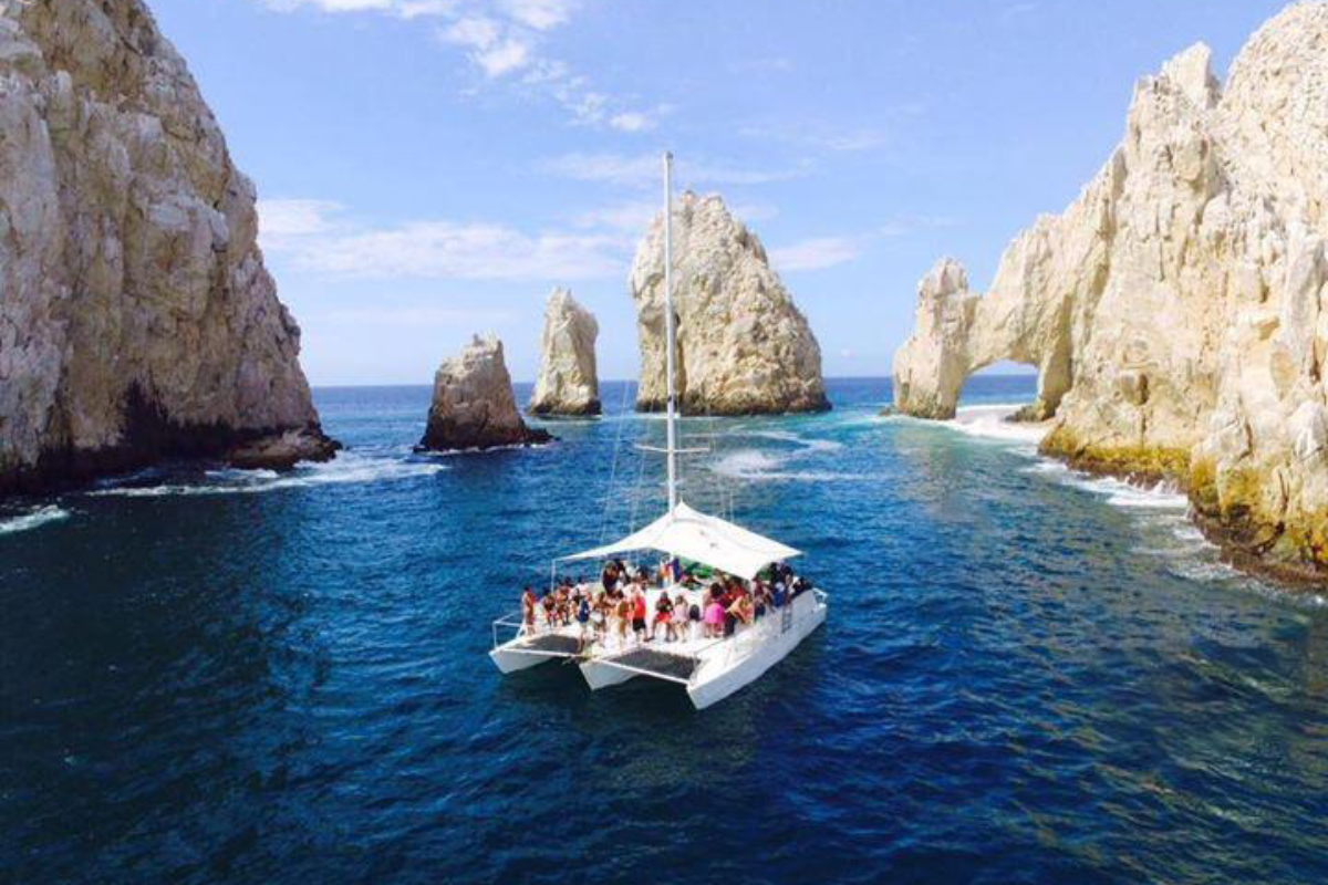 Sailing trimaran with guests aboard near the Arch at Land's End in Cabo San Lucas