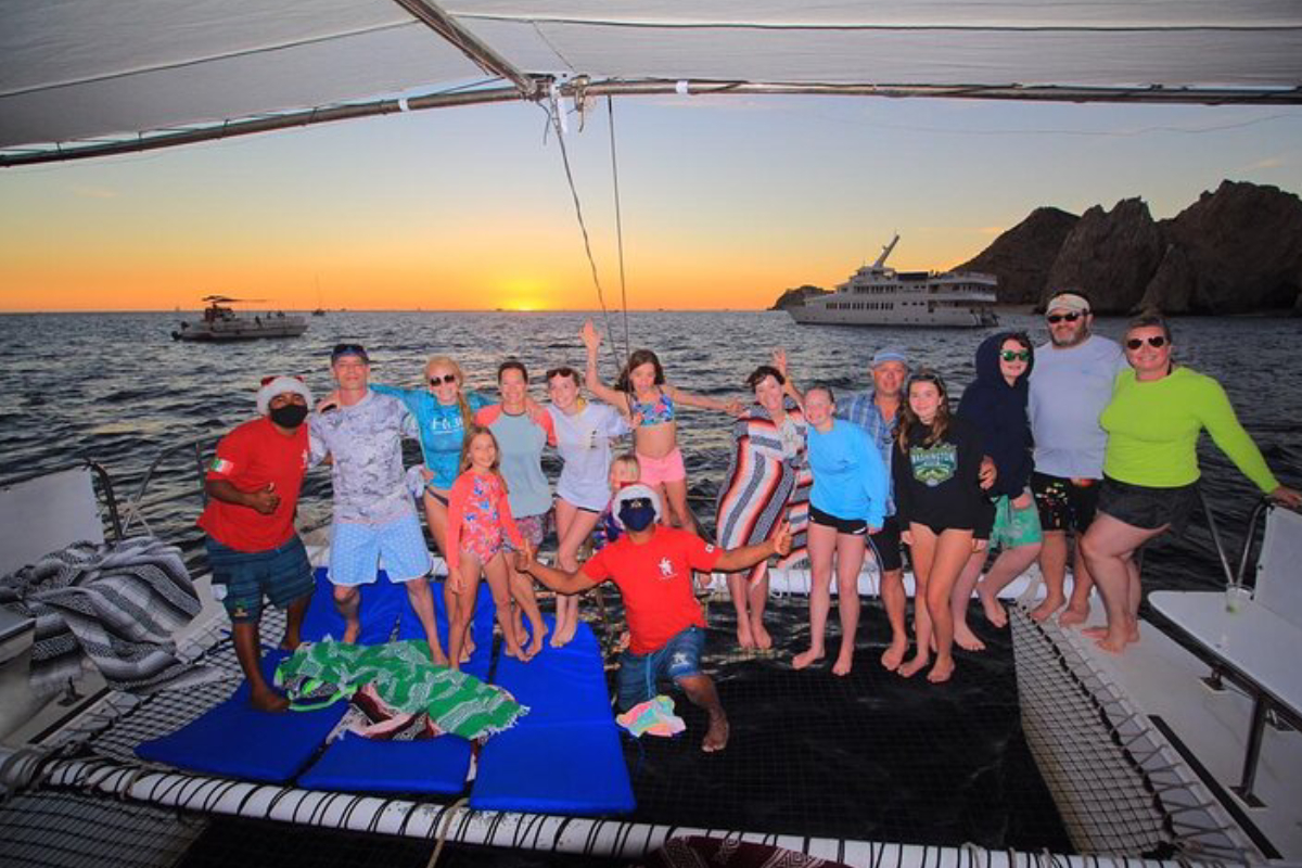 A private group posing on the bow nets of their chartered catamaran at sunset