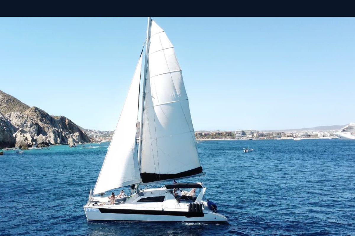 Leopard sailing catamaran under full sail off the Cabo San Lucas shoreline