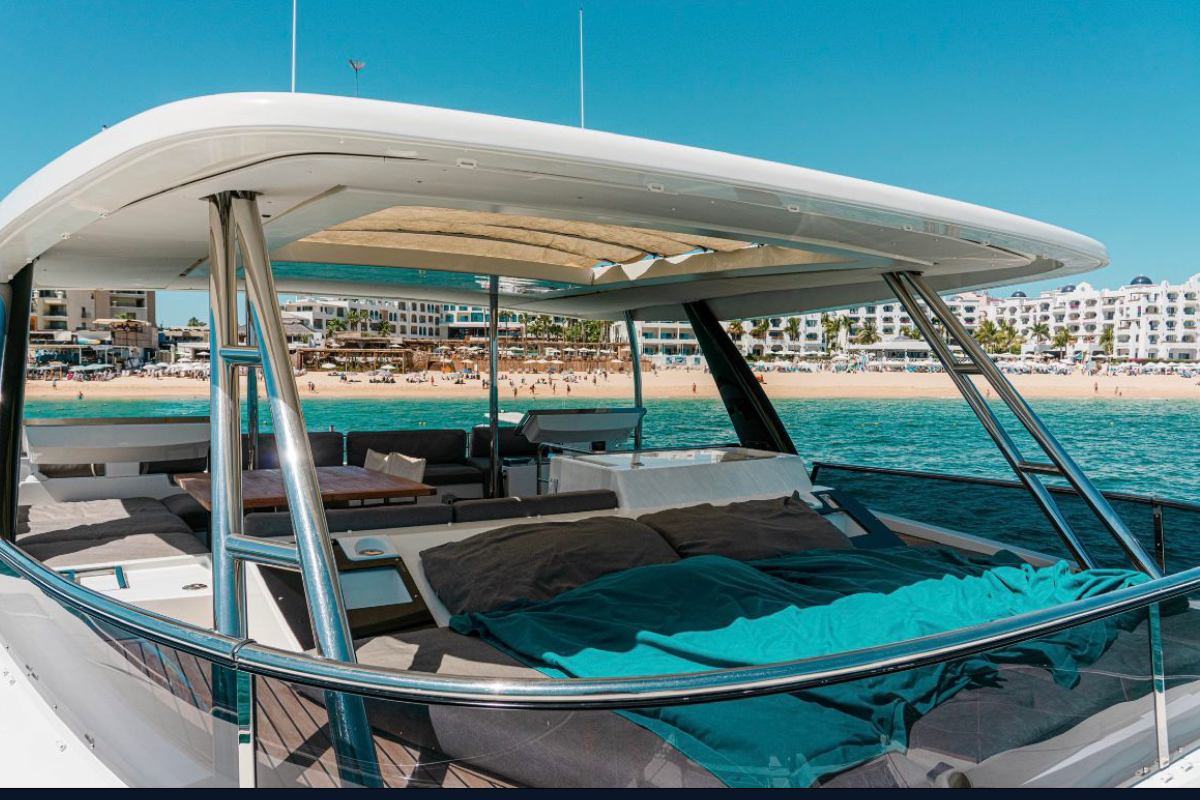 Shaded aft deck lounge of a luxury catamaran with the Cabo San Lucas beachfront behind