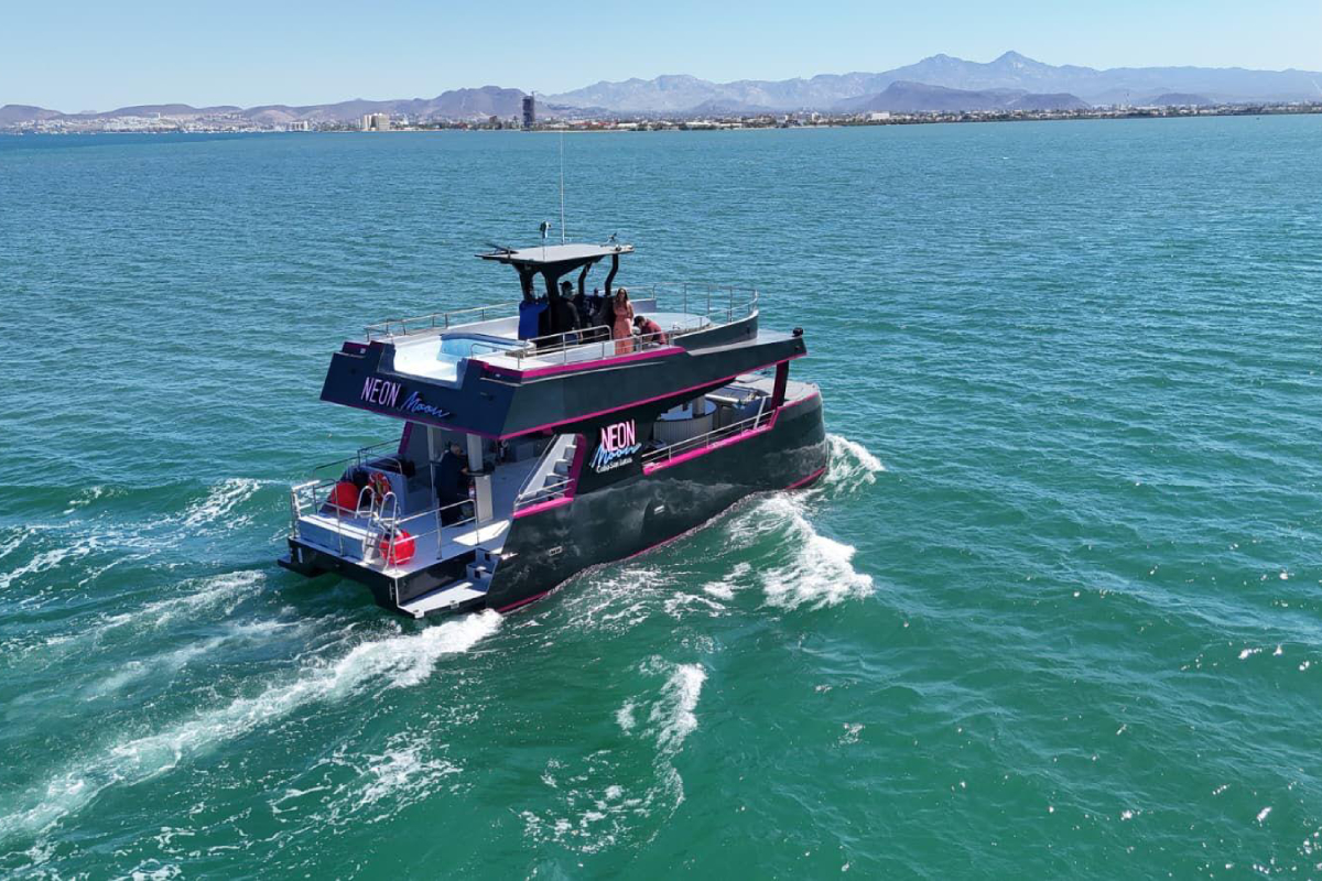 The Neon Moon party catamaran cruising the bay of Cabo San Lucas with guests on both decks