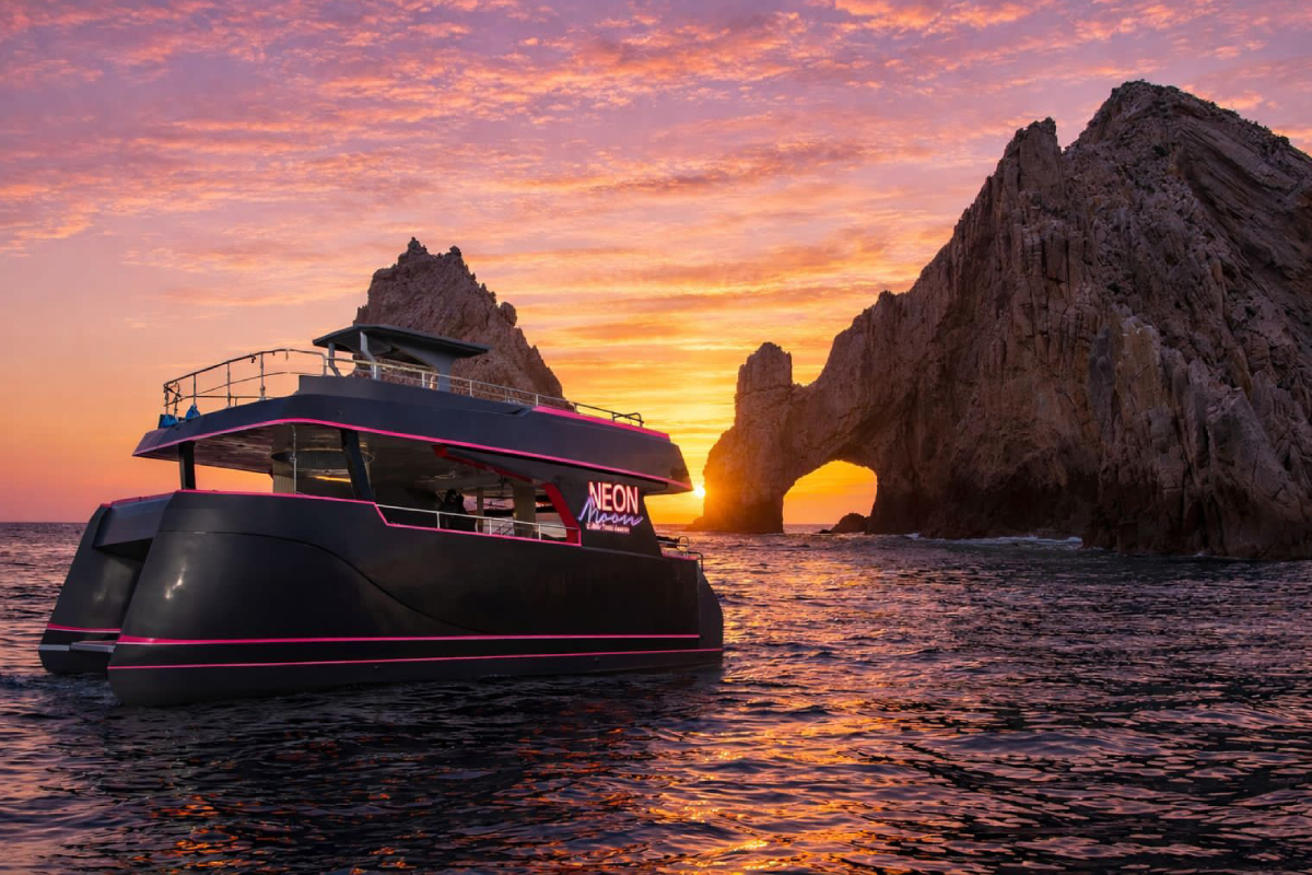 Neon Moon party catamaran with LED lighting at sunset near the Cabo Arch